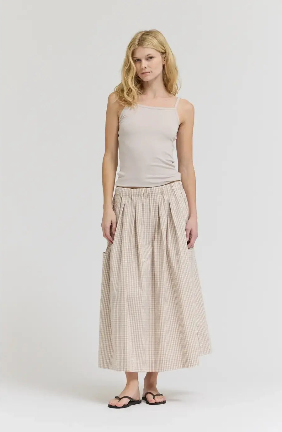Woman wearing a beige sleeveless top and checkered skirt on a white background